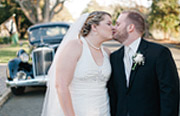 Bride and groom kissing with vintage car behind them