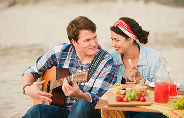 Party at the beach - couple playing guitar and eating